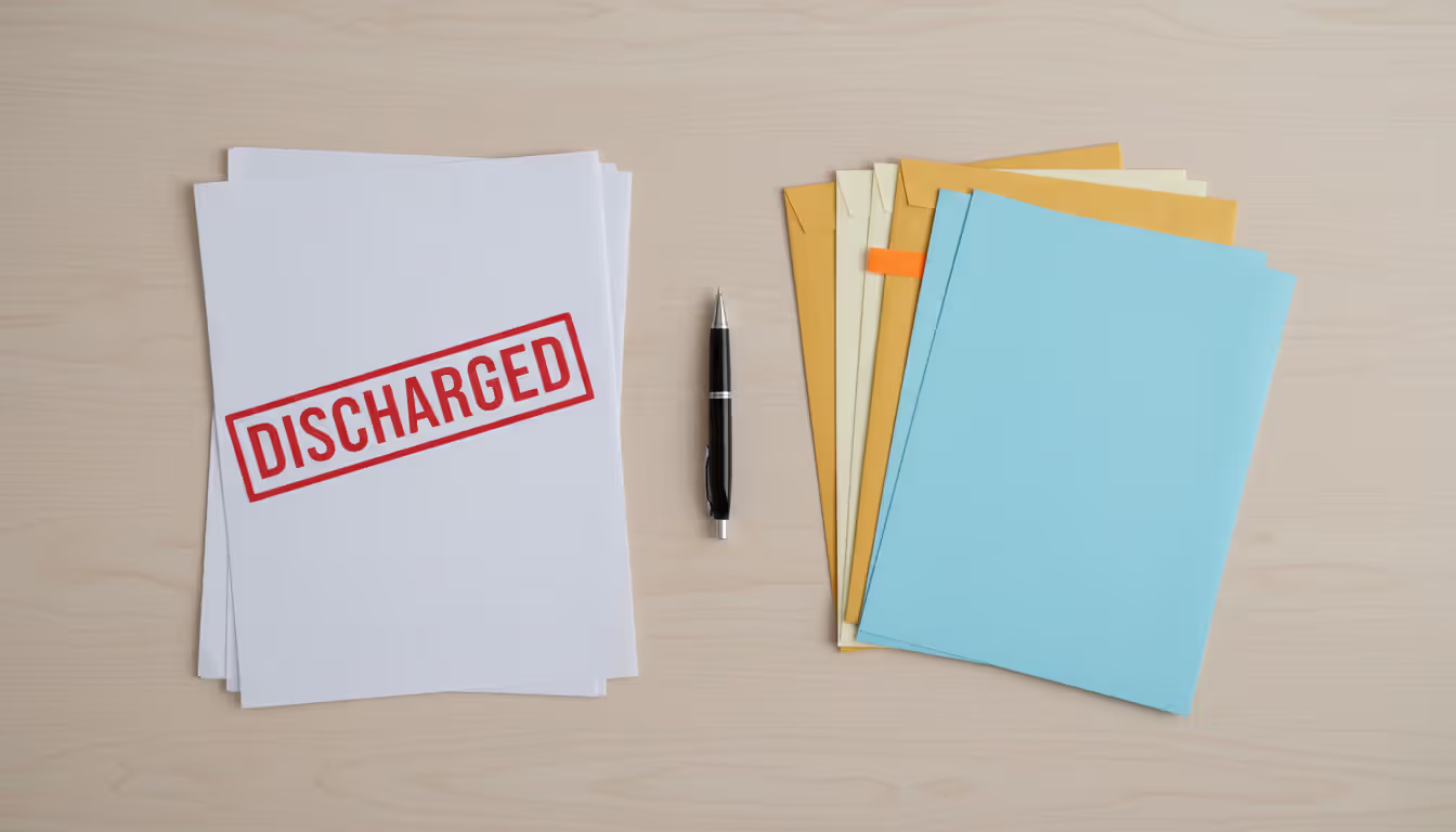 A top-down view of a light wooden desk with neatly organized stacks of documents and envelopes in white yellow and blue colors, one stack stamped with a red DISCHARGED mark, another marked with an orange bookmark, and a pen lying nearby