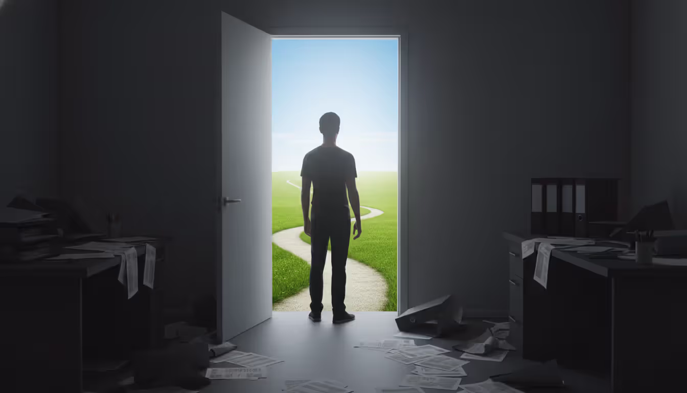 A person standing at an open doorway looking out into bright sunlight and a green path ahead with a dark room full of scattered papers behind them